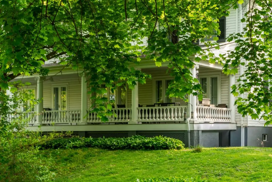 A front porch with railings seen through tree branches at the front of a house