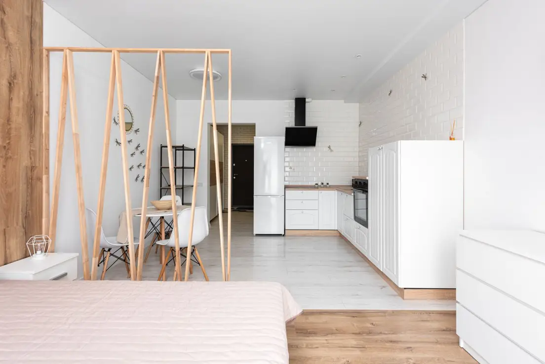 A studio apartment with a wood A-frame room divider separating the bed from a small dining area