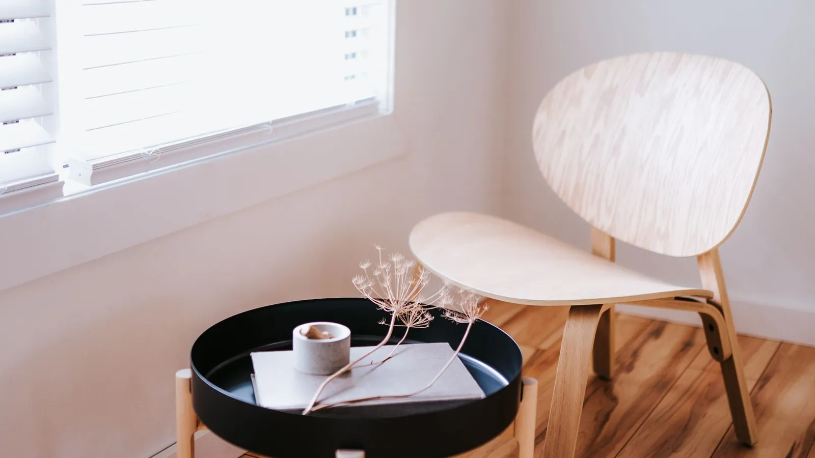 A simple bent-wood chair and round wooden side table with dried flowers in a minimal room