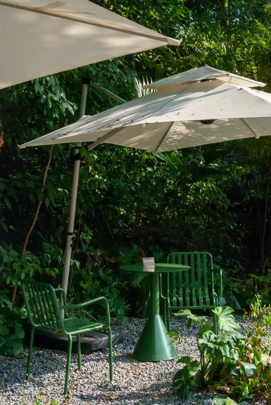Green outdoor bistro chairs and a table with market umbrellas set on a gravel patio