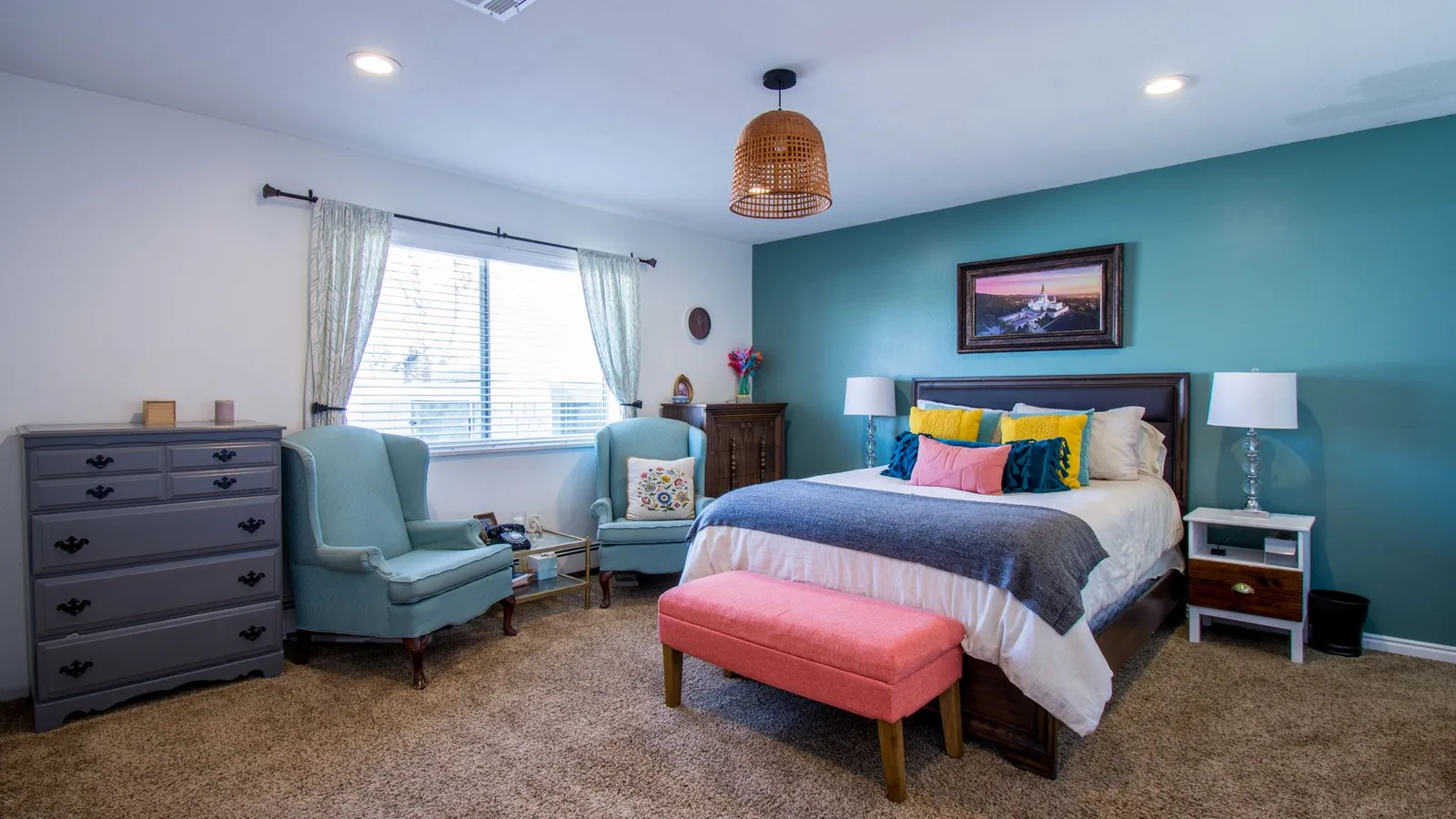 A bedroom with a repainted grey dresser, teal accent wall, and colorful throw pillows