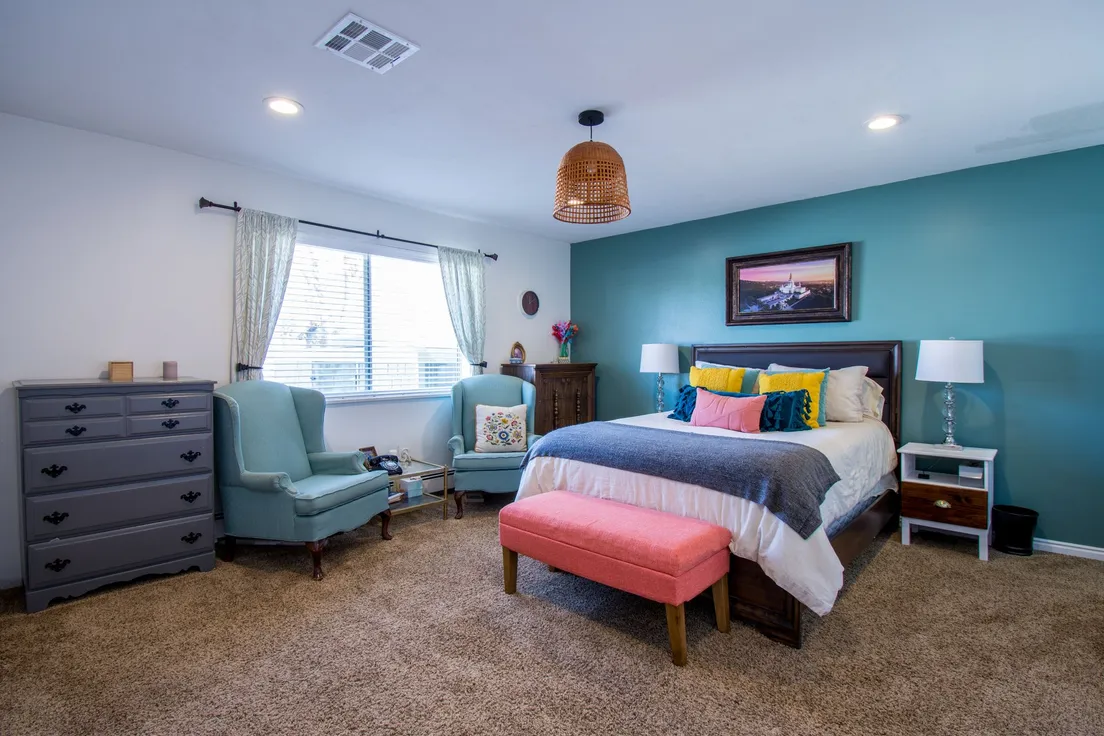 A bedroom with a repainted grey dresser, teal accent wall, and colorful throw pillows