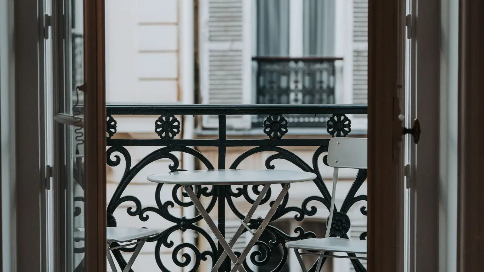 A small round bistro table with two folding chairs seen through open French doors onto a Paris apartment balcony