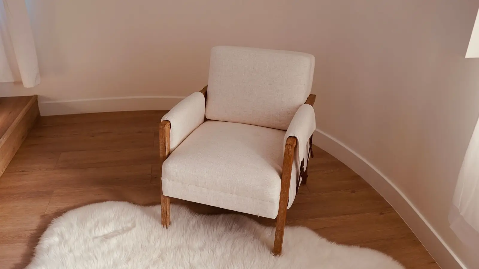 A cream linen armchair with a wood frame on a light wood floor with a sheepskin rug