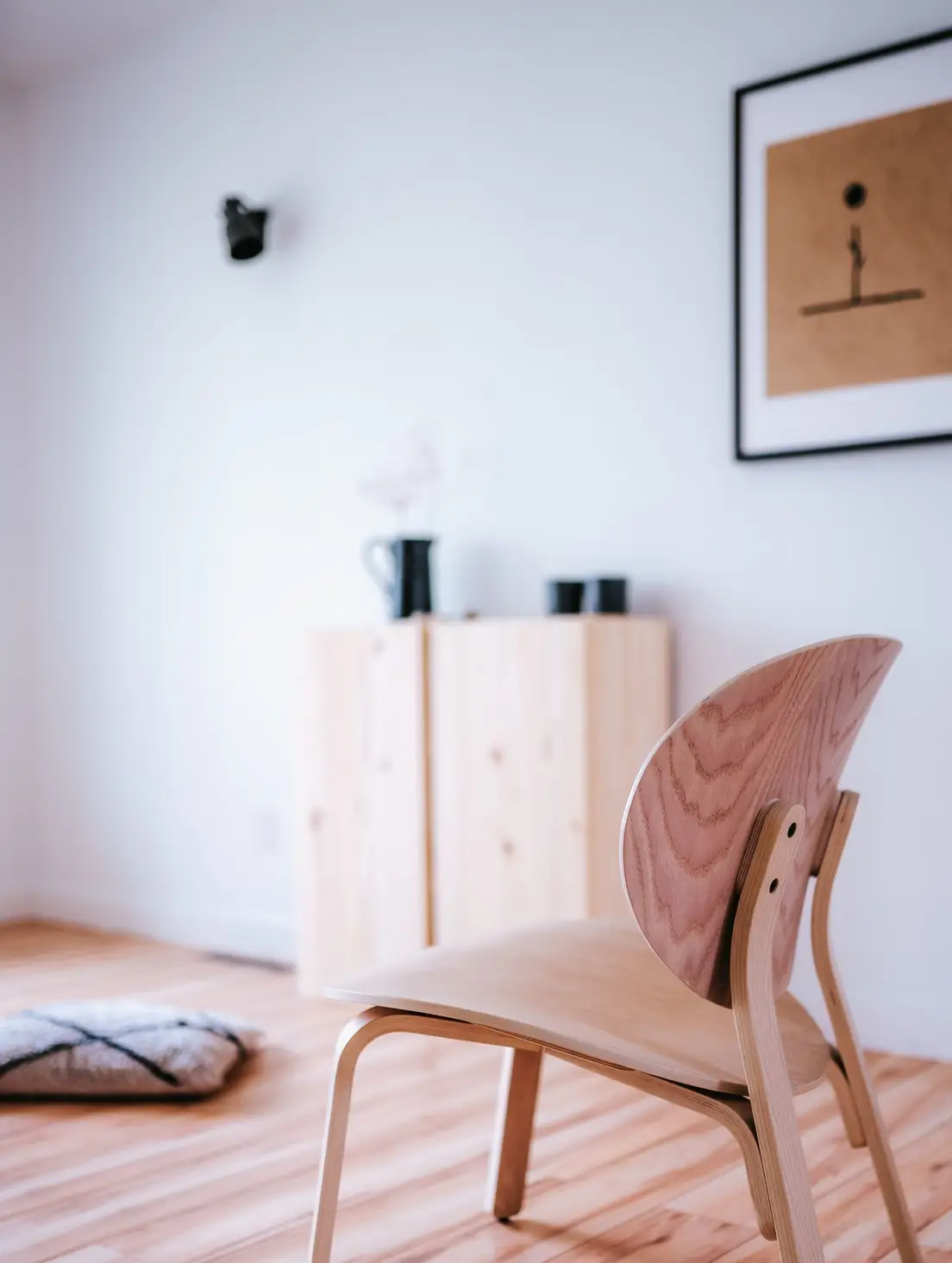 A low, curved wood chair beside a wall-mounted cabinet in a light-filled minimalist room