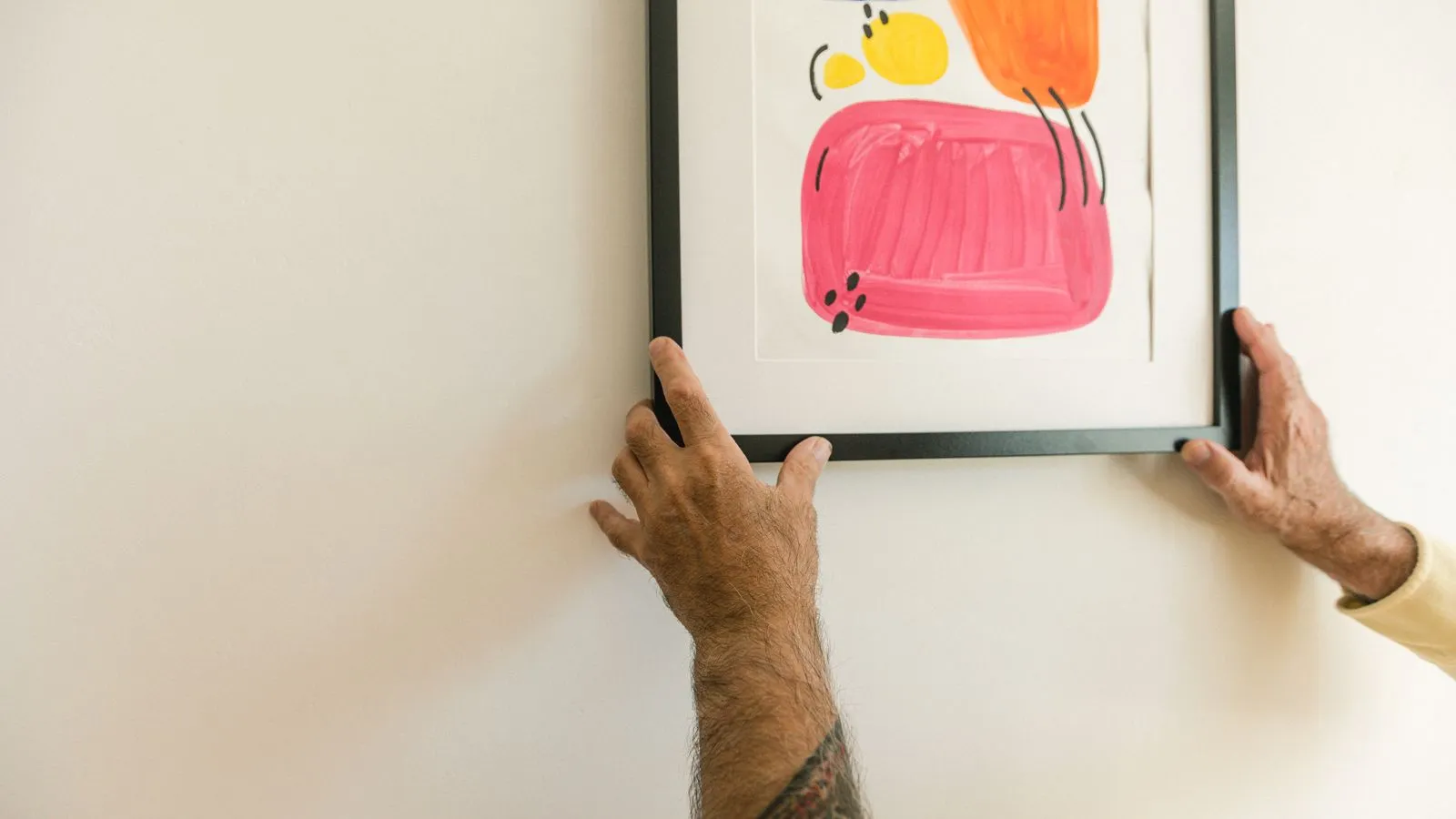 Hands hanging a bright abstract print in a black frame on a white wall for a no-nail gallery wall