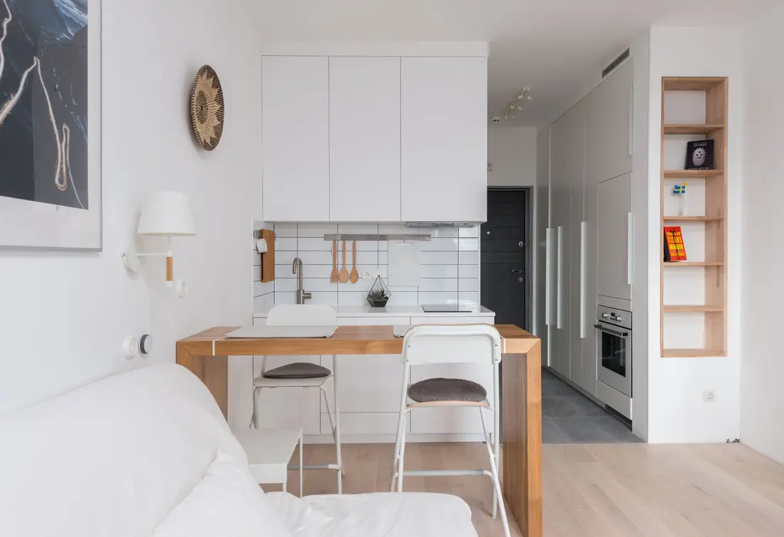 A one-wall galley kitchen with white cabinetry keeping the rest of a small apartment's floor plan open