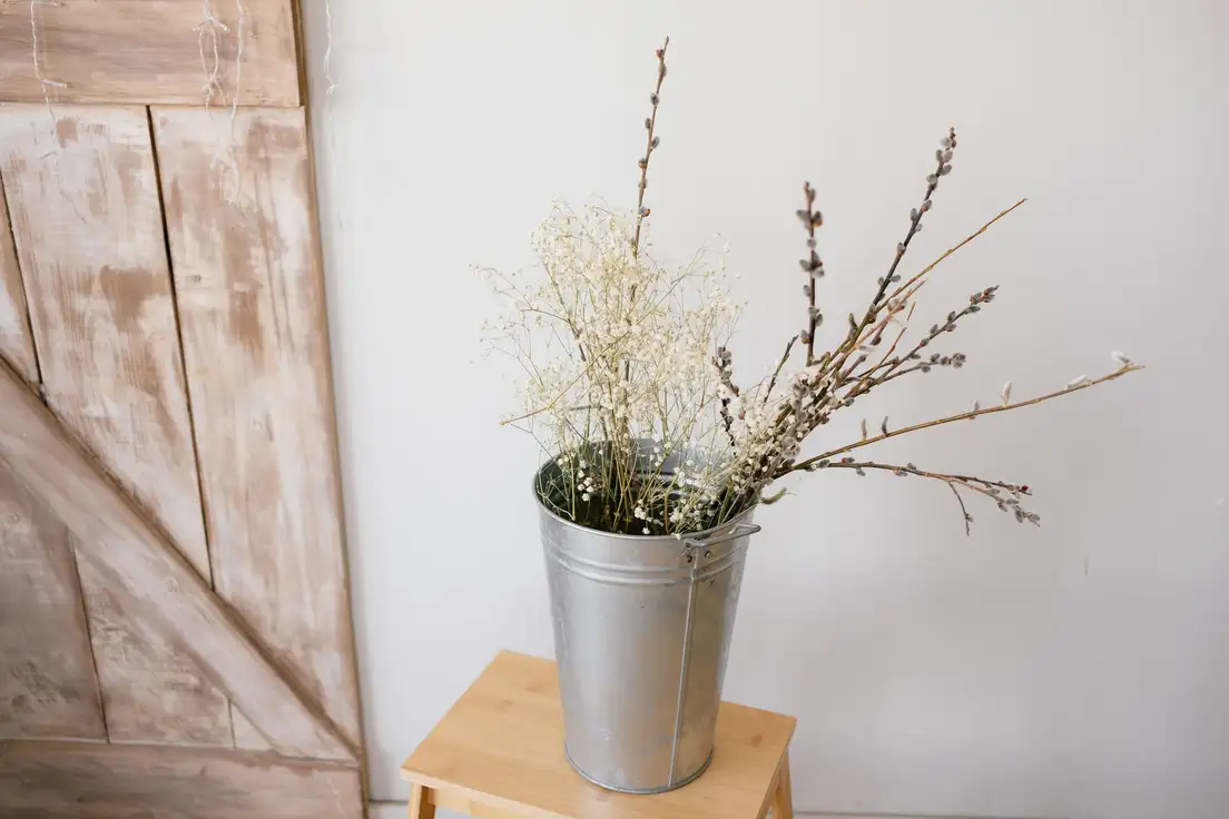 A galvanized metal bucket holding dried branches and baby's breath beside a weathered wood barn-door panel, a budget farmhouse decor idea