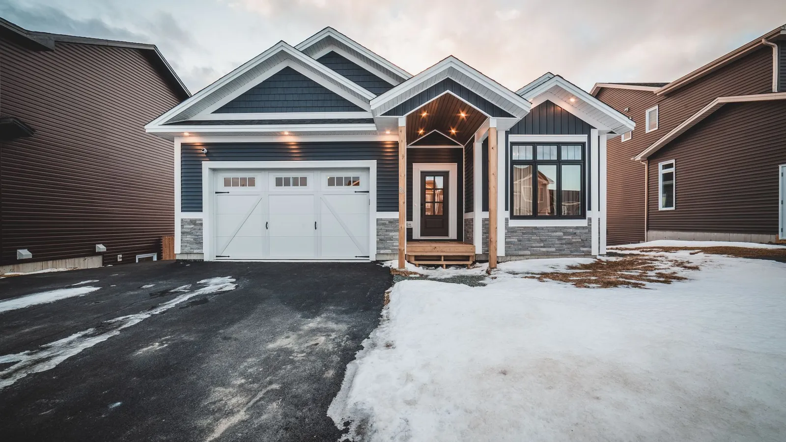 A ranch house exterior at dusk with a dark garage door matching the dark siding
