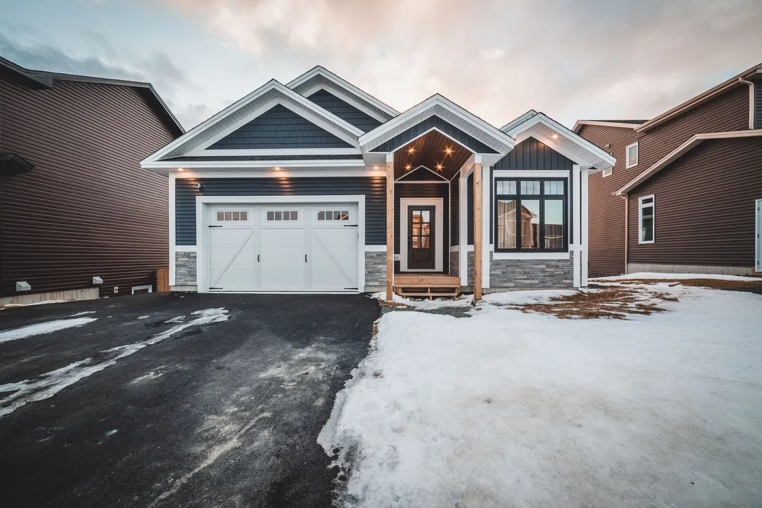 A ranch house exterior at dusk with a dark garage door matching the dark siding