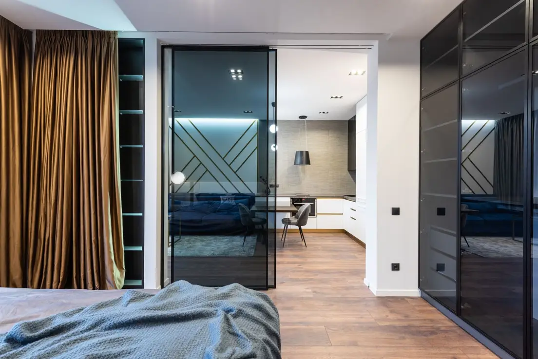 A modern apartment with a black-framed glass panel dividing the bedroom from the kitchen