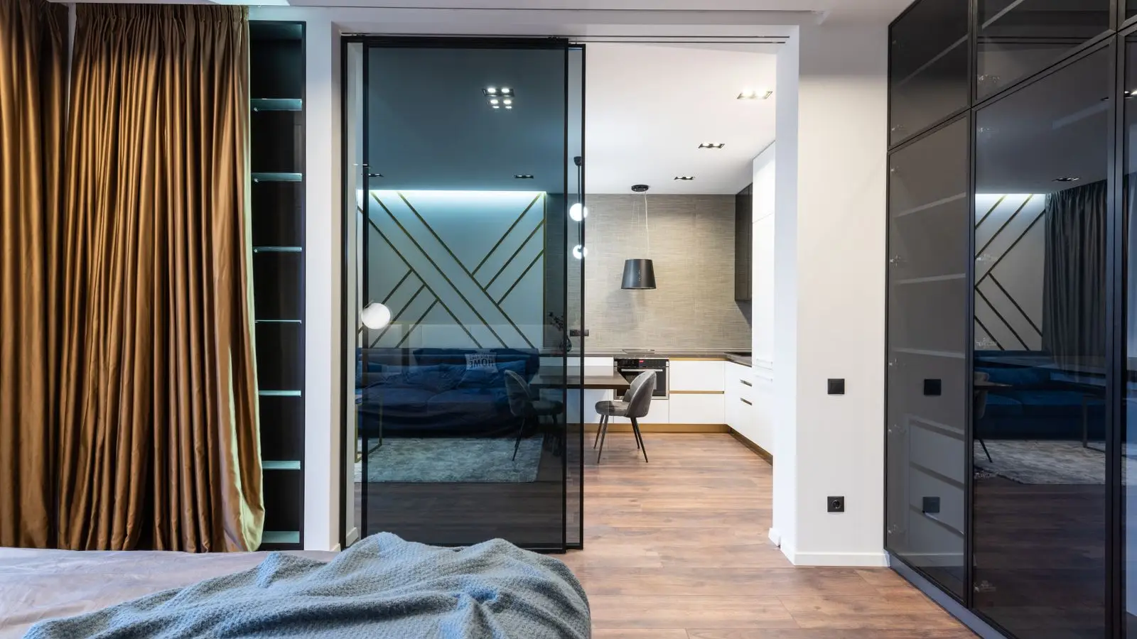 A modern apartment with a black-framed glass panel dividing the bedroom from the kitchen