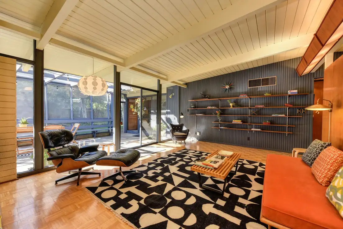 A mid-century modern living room with floor-to-ceiling glass walls and a sliding door opening onto a patio courtyard