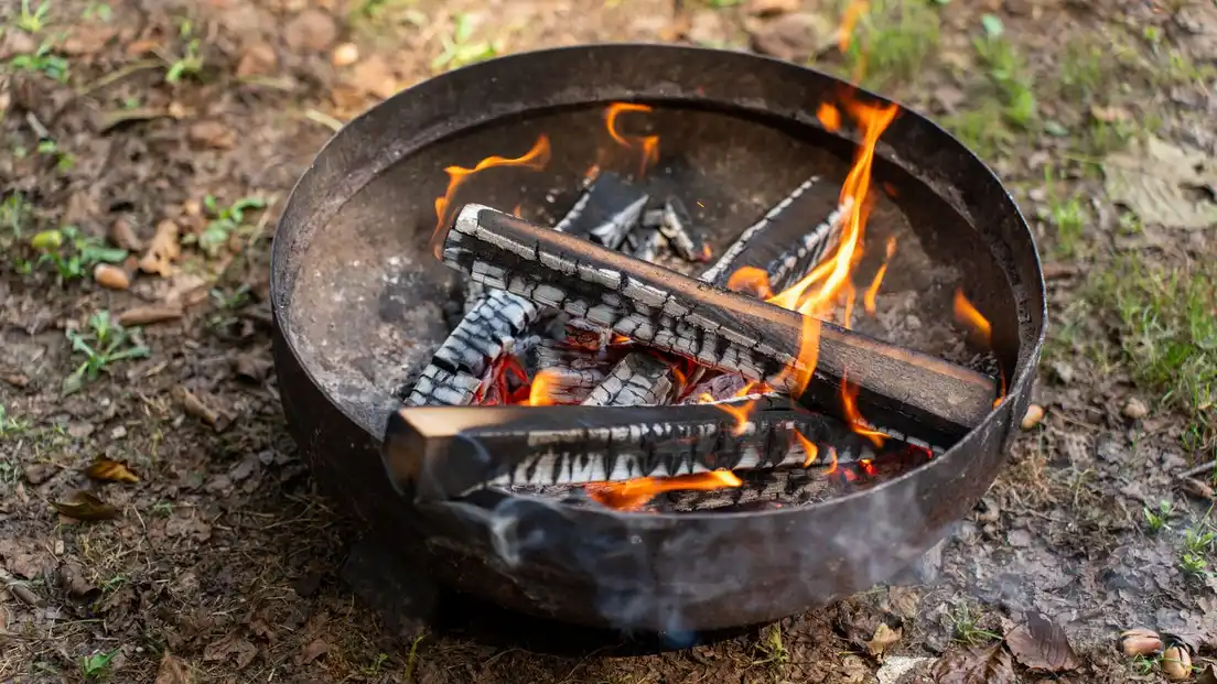 A cast-iron fire pit bowl burning on bare grass and dirt, scorching the lawn