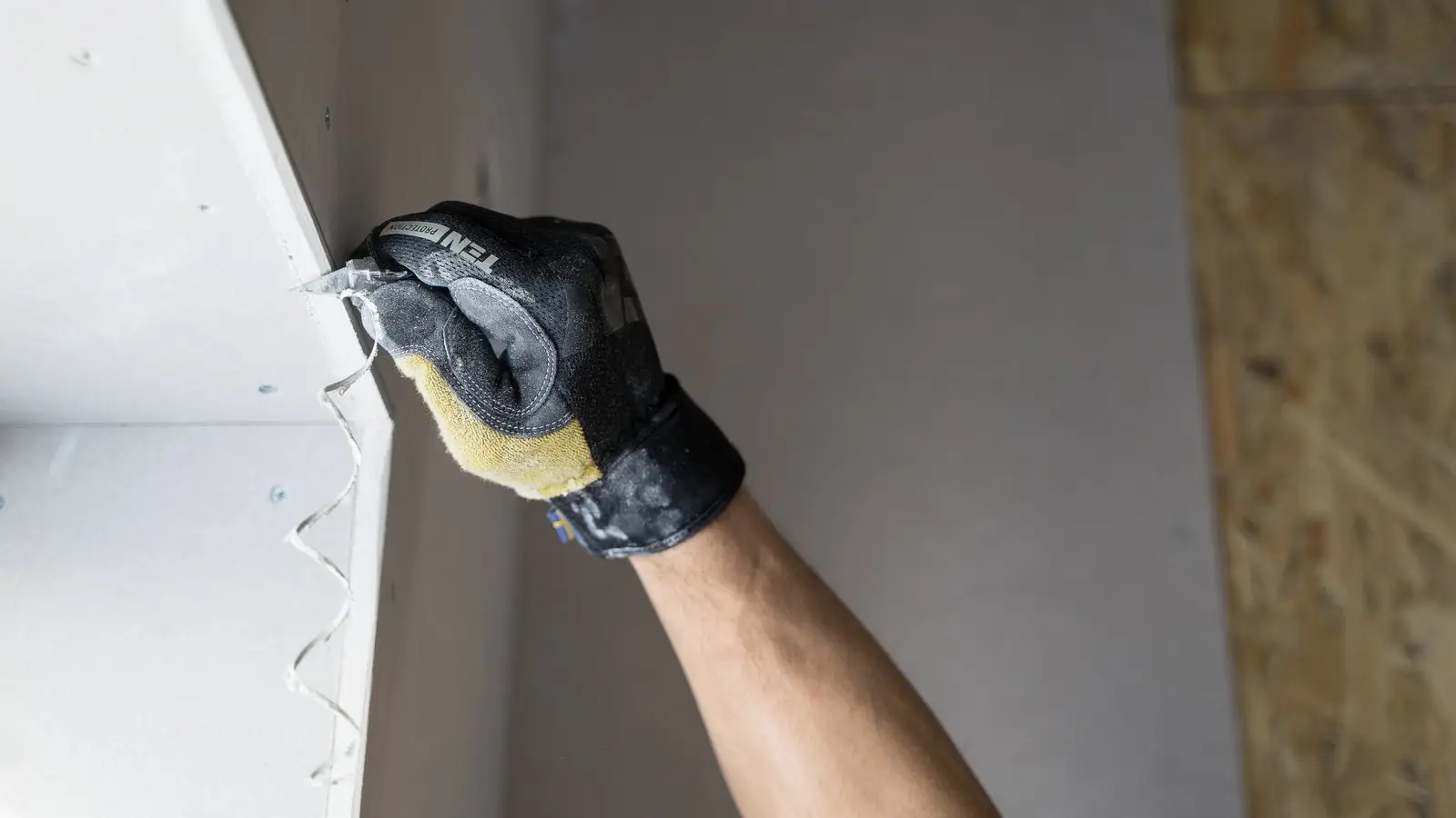 A gloved hand cutting a drywall panel edge during installation of a temporary wall