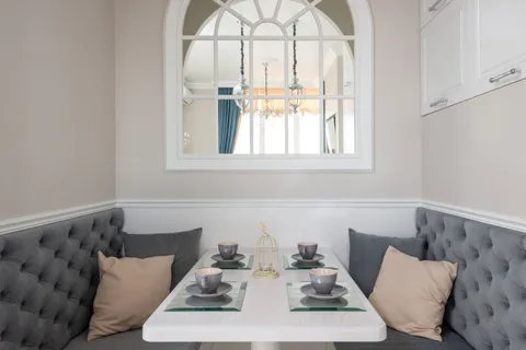 A small kitchen nook with a curved gray tufted banquette bench, a white table, and an arched window