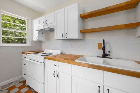 A small white kitchen with wood countertops, open shelving, and a farmhouse sink