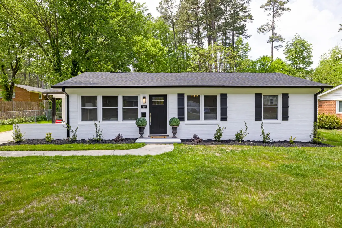 A single-story ranch house exterior with white brick, black shutters, and a matching black front door