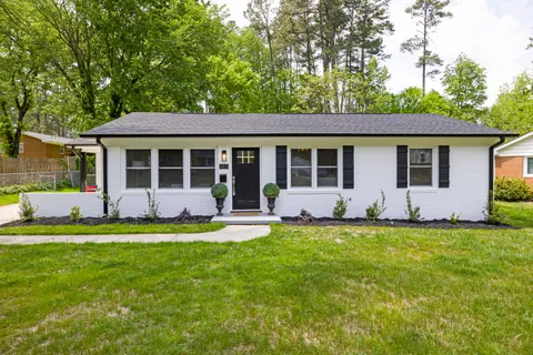 A single-story ranch house exterior with white brick, black shutters, and a matching black front door