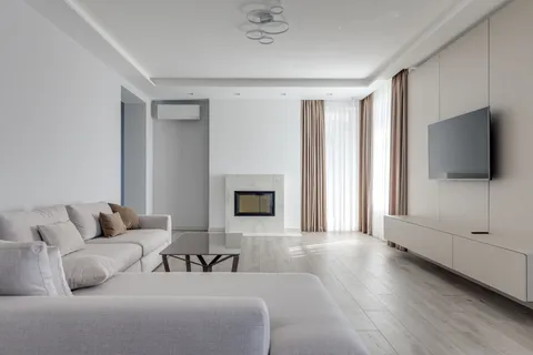 A modern minimalist living room with a gray sectional sofa, marble fireplace, and wall-mounted TV in warm neutral tones