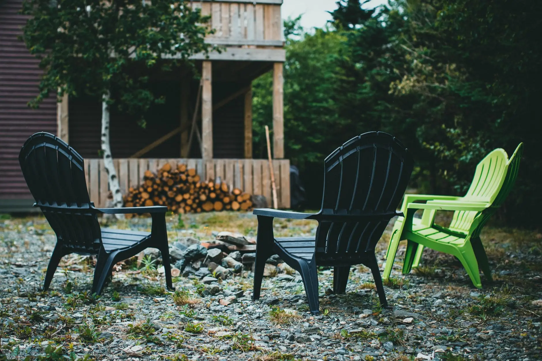 Adirondack chairs around a fire ring in a gravel backyard with no grass