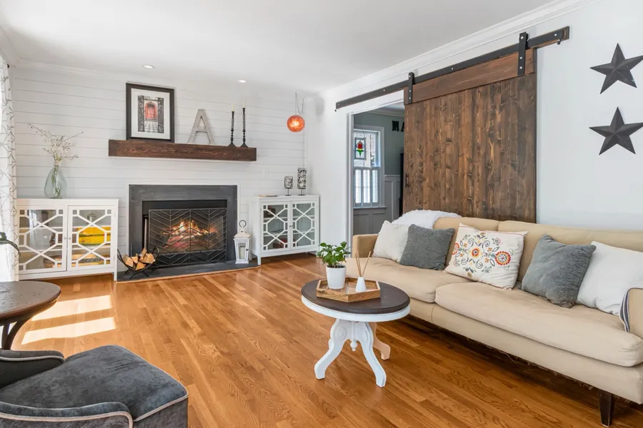 A modern farmhouse living room with white shiplap walls, a sliding wood barn door, and a beige slipcovered sofa