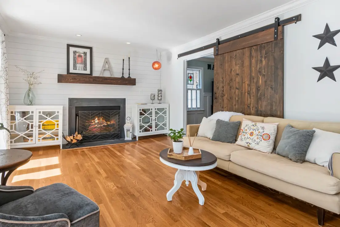 A modern farmhouse living room with white shiplap walls, a sliding wood barn door, and a beige slipcovered sofa