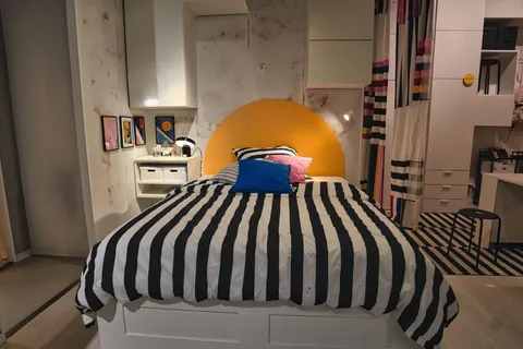 A dopamine decor bedroom with striped black-and-white bedding, a yellow arch headboard, and a wall of colorful prints
