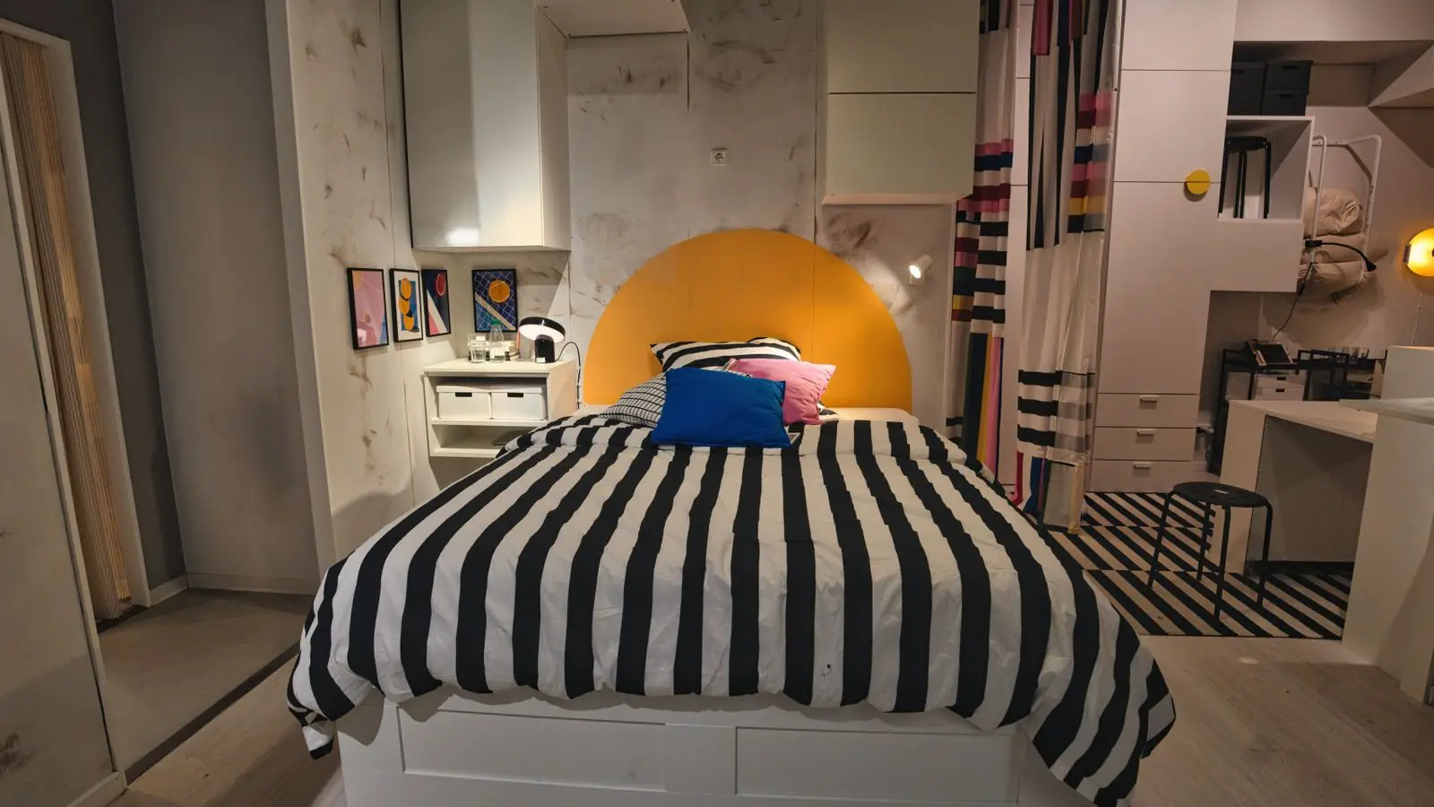 A dopamine decor bedroom with striped black-and-white bedding, a yellow arch headboard, and a wall of colorful prints