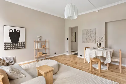 An organic modern living room with warm beige walls, oak floors, a round pedestal table, and a cream boucle pouf