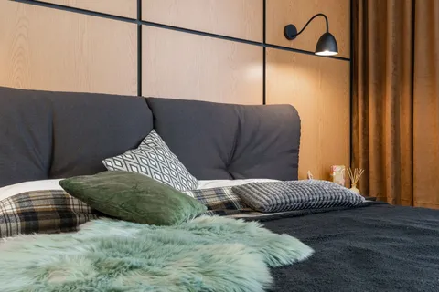 A warm, layered bedroom with wood wall paneling and a black wall sconce