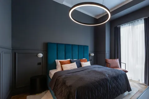A masculine bedroom with charcoal walls, a teal upholstered headboard, and a ring pendant light