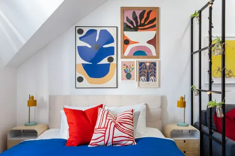 A dopamine decor bedroom with a colorful gallery wall, a red striped throw pillow, and bold blue bedding