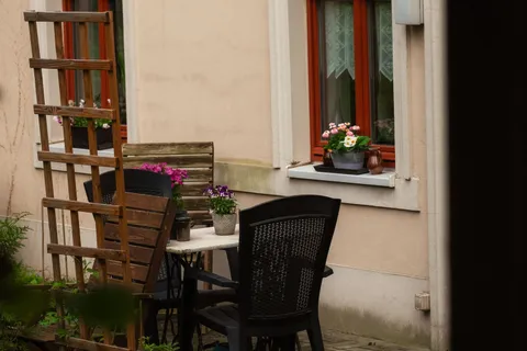 A small backyard patio with a wooden trellis, potted flowers, and a simple bistro table and chairs