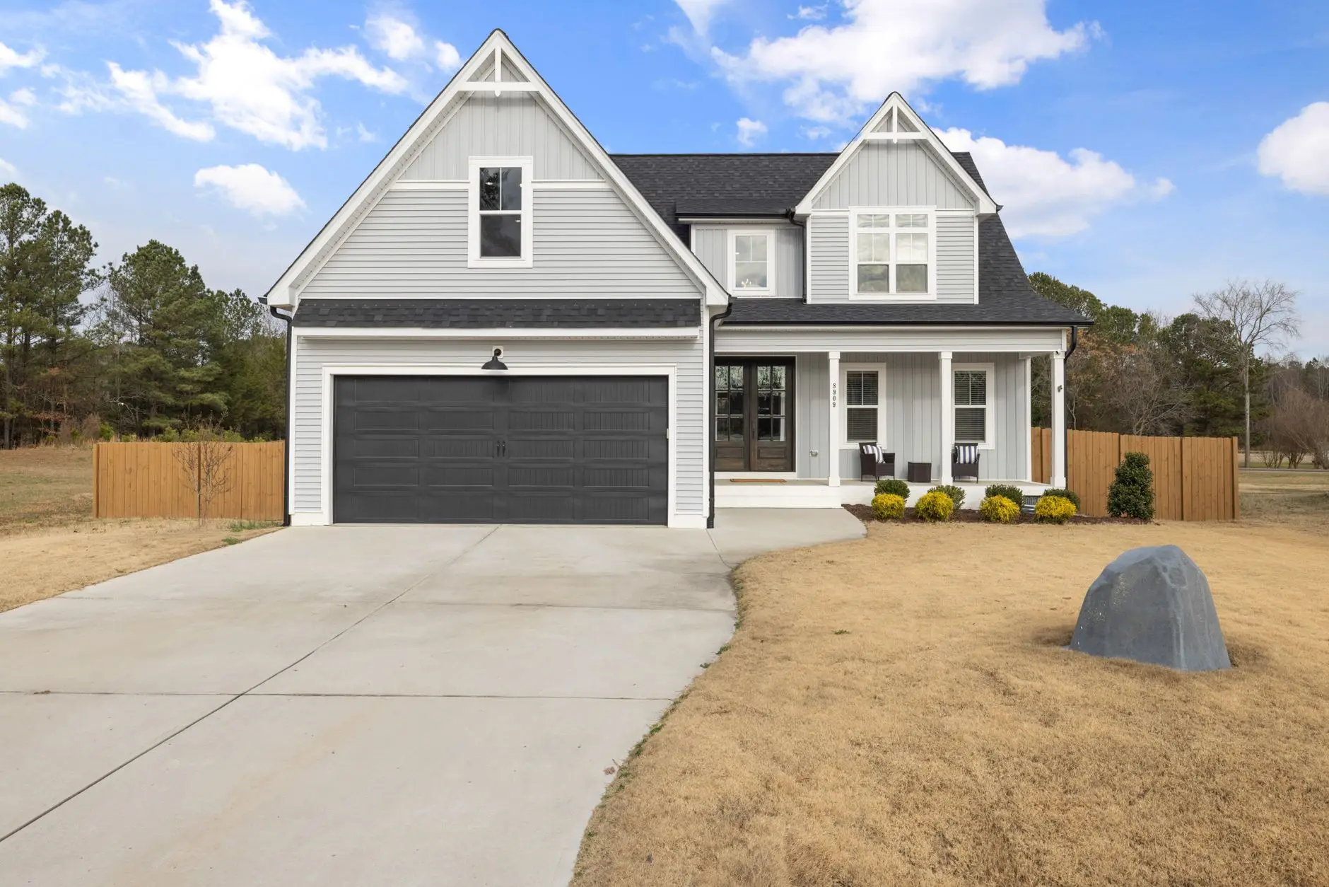 A modern farmhouse exterior with warm-white board-and-batten gables, black windows, and a covered front porch