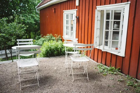 A pea gravel patio with white bistro chairs and a round table against a red house