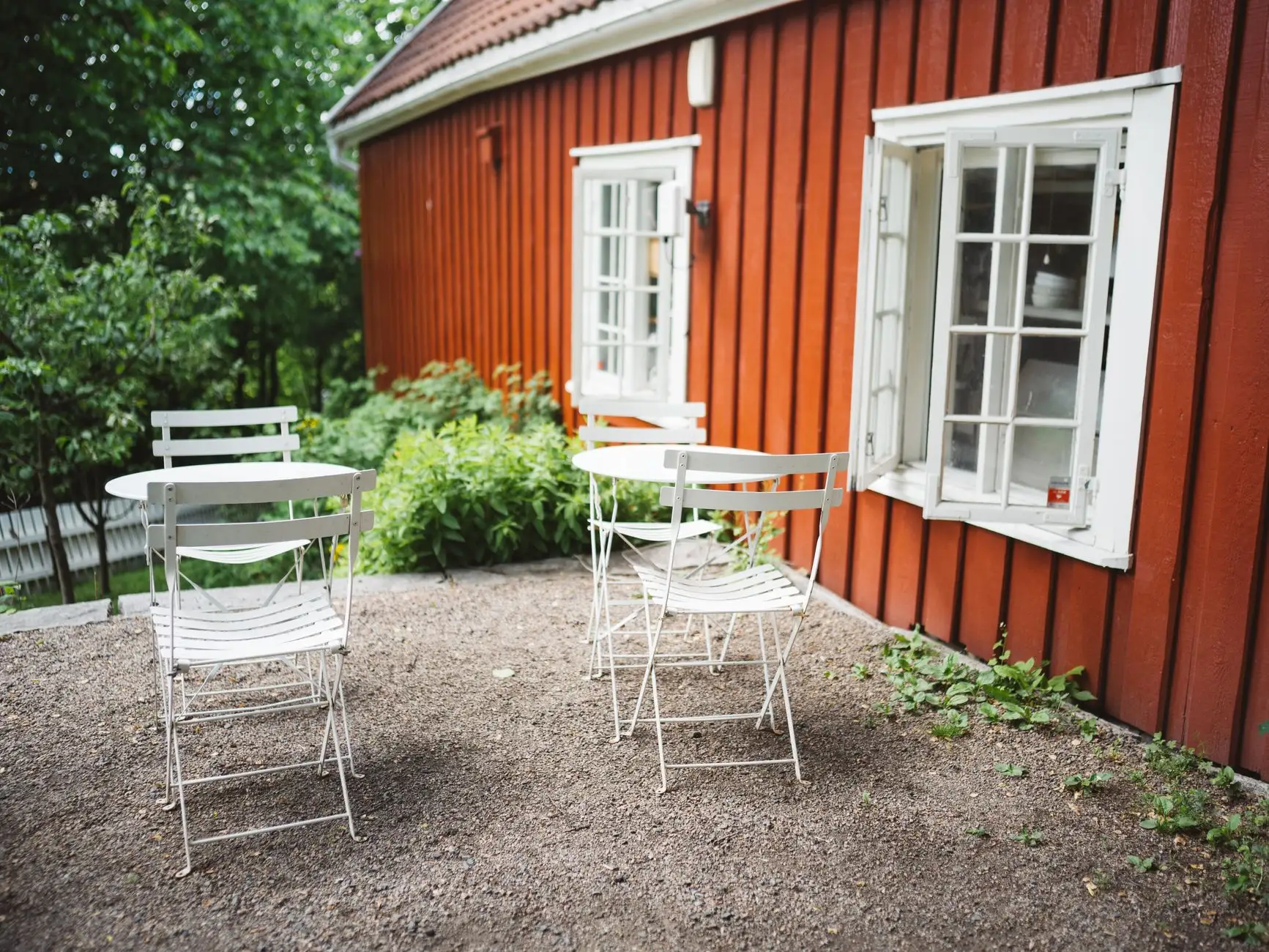 A pea gravel patio with white bistro chairs and a round table against a red house