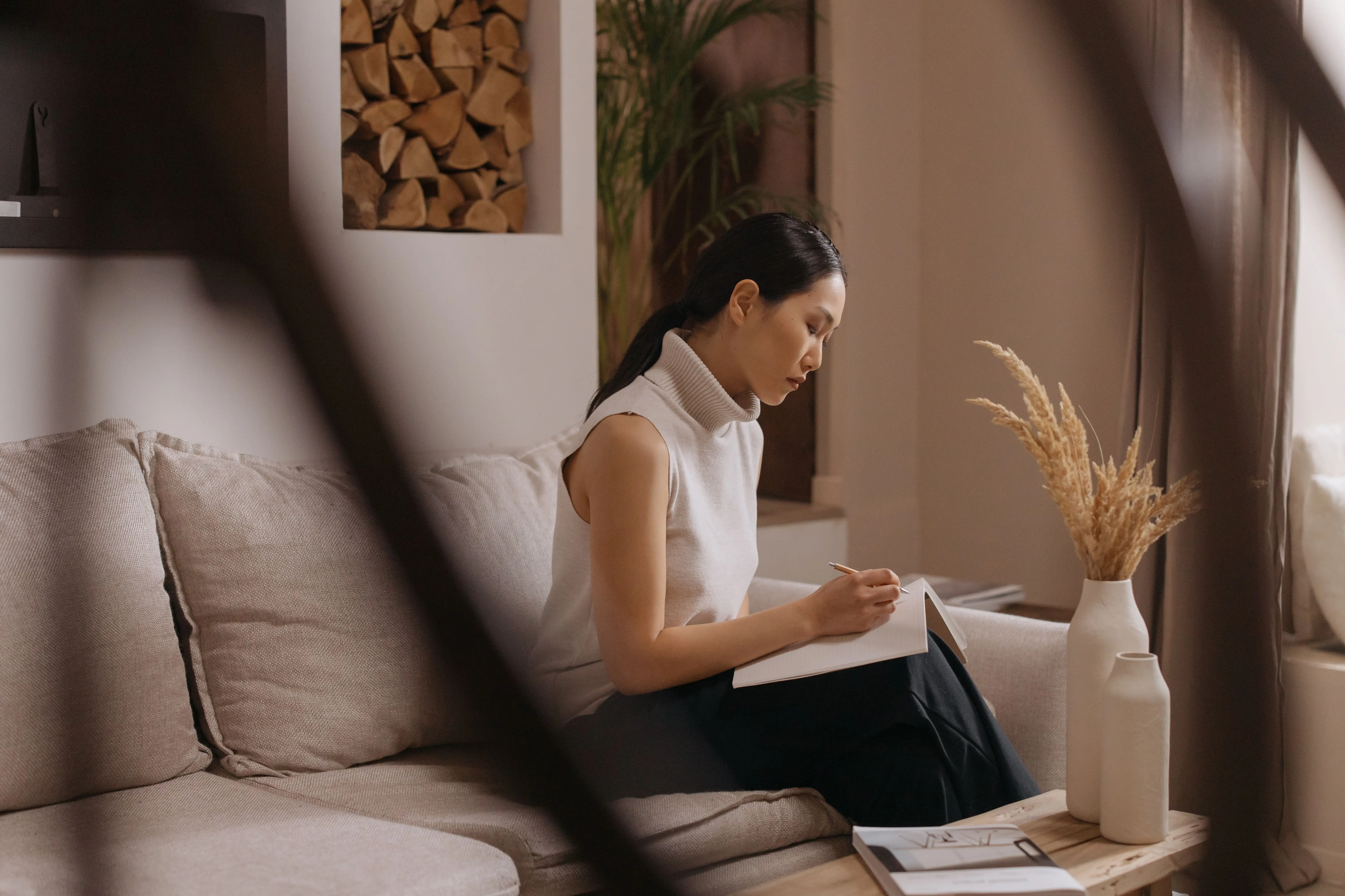 A woman sitting on a low gray sofa in a Japandi-style living room with warm wood tones and natural light