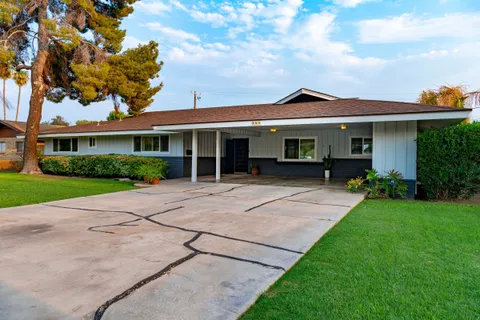 A mid century modern ranch house with a long low hip roof, an open carport, gray board-and-batten siding, and a painted brick base