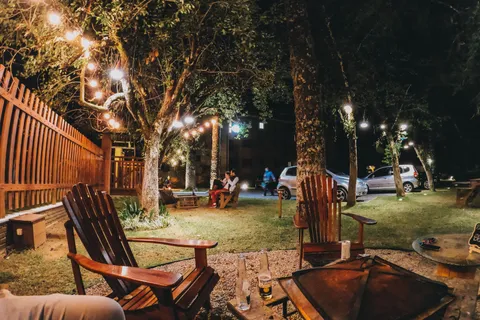 Adirondack chairs around a backyard fire pit strung with string lights at a small evening party