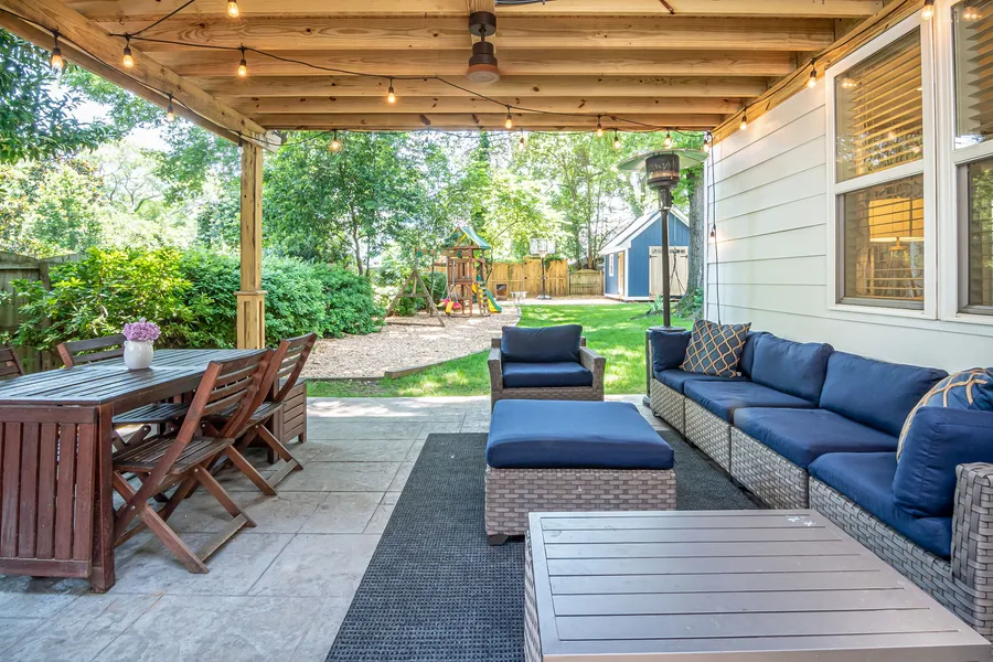 A backyard covered patio with a sectional sofa, string lights, and a ceiling fan