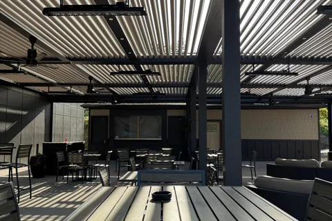 A freestanding aluminum patio cover with a louvered roof over an outdoor dining and lounge area
