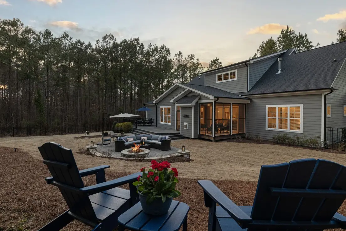 A modern backyard with a fire pit seating area, curved sofa, and black Adirondack chairs at sunset