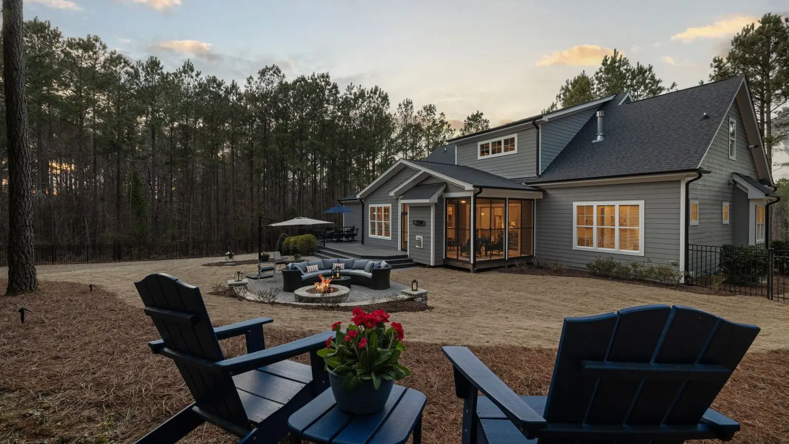 A modern backyard with a fire pit seating area, curved sofa, and black Adirondack chairs at sunset