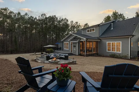 A modern backyard with a fire pit seating area, curved sofa, and black Adirondack chairs at sunset