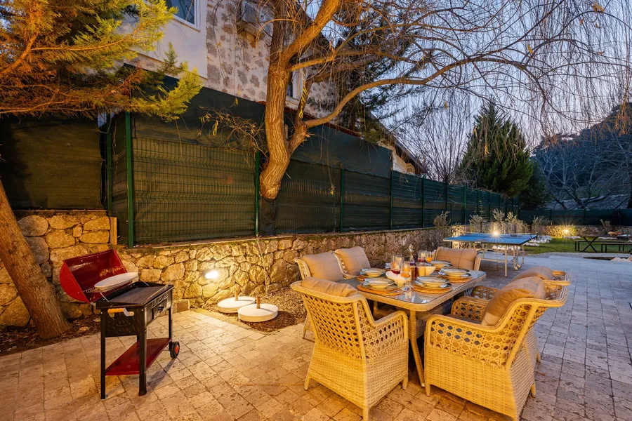 Outdoor dining table and charcoal grill set up in a backyard BBQ area at dusk