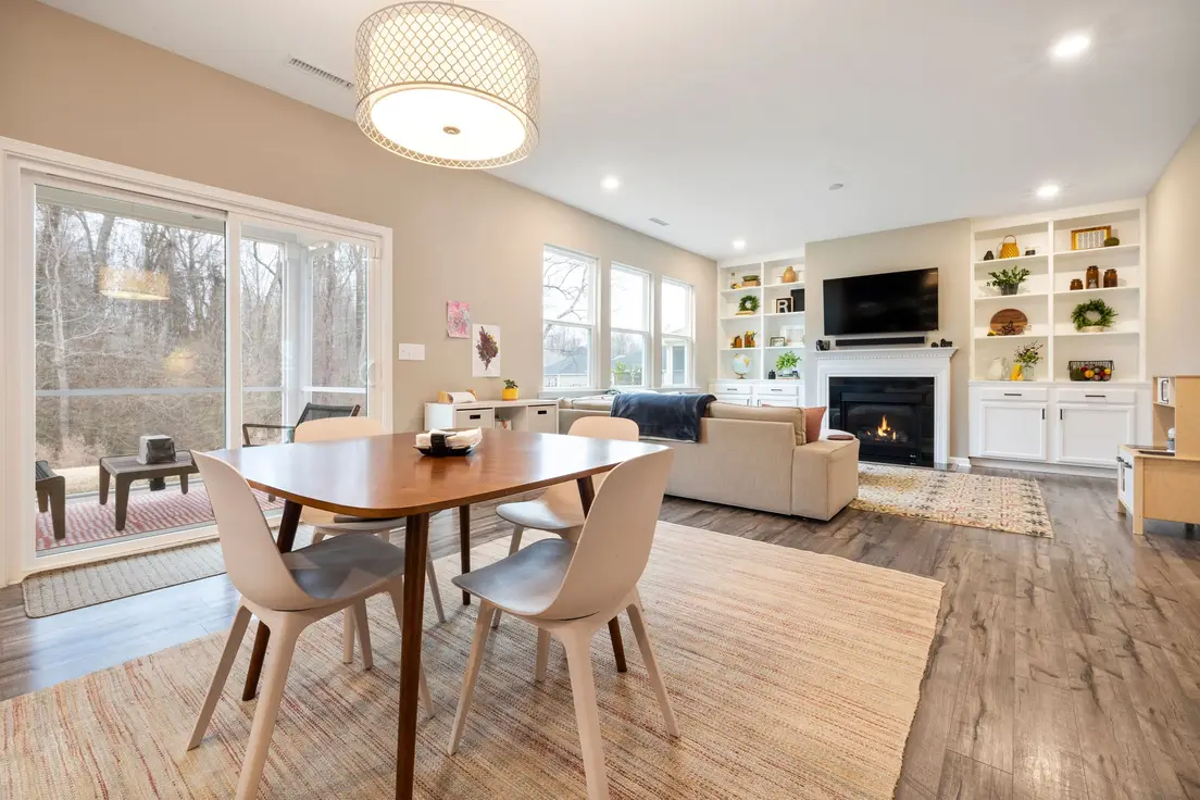 A small living room dining room combo with a wood dining table on a striped rug in front of a sectional, fireplace, and built-in shelves