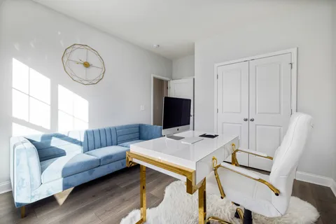 A white desk and office chair set beside a blue velvet sofa, an office living room combo in one bright room