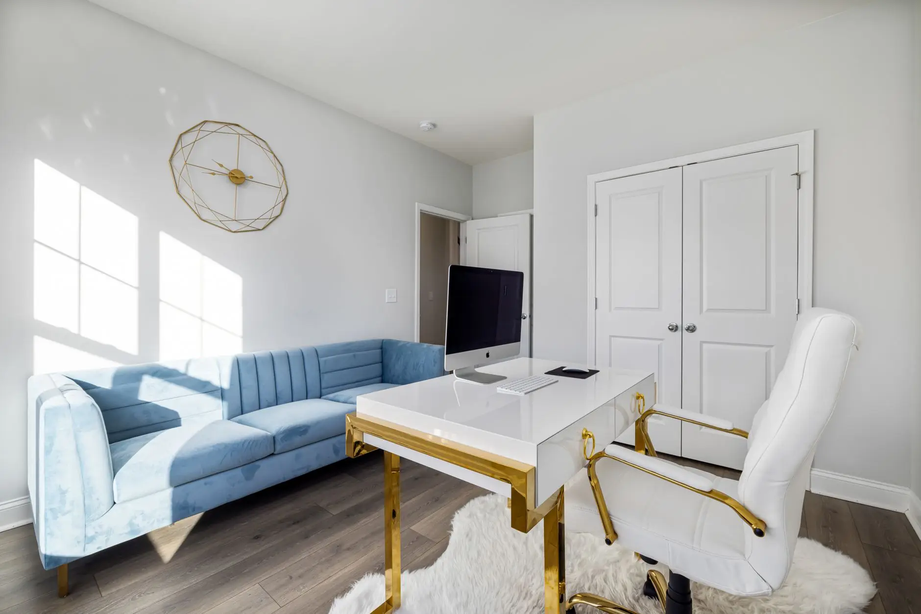 A white desk and office chair set beside a blue velvet sofa, an office living room combo in one bright room
