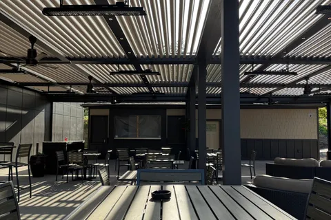 A freestanding aluminum patio cover with a louvered roof over an outdoor dining and lounge area